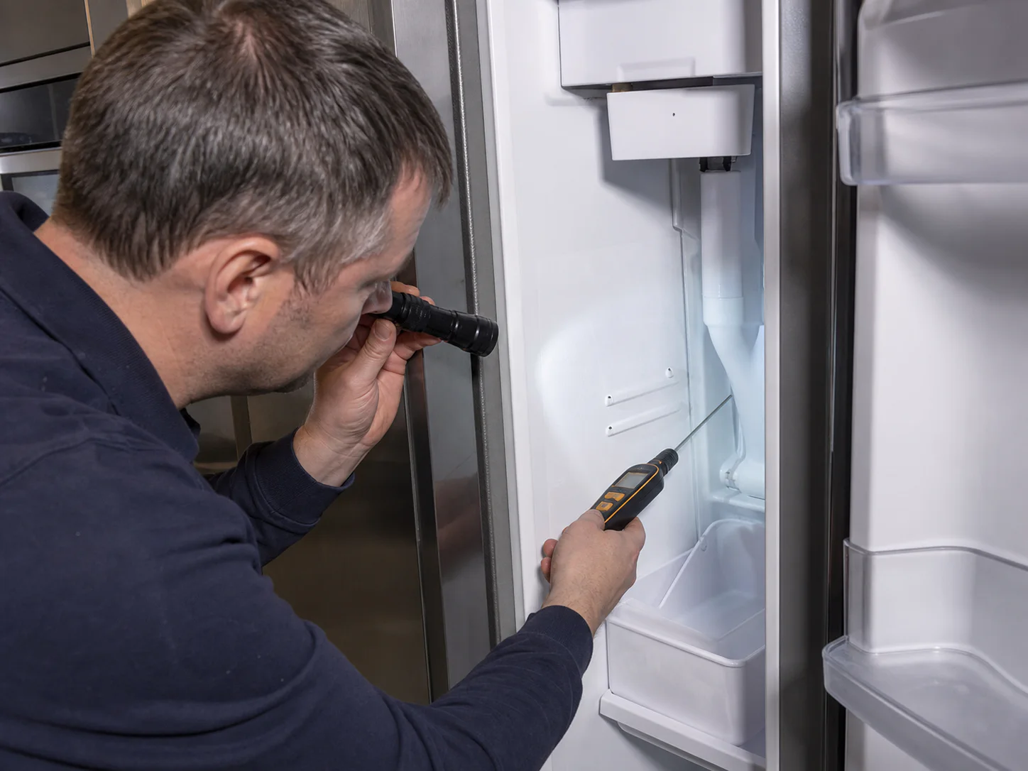 Technician inspecting an empty ice bin and fill tube in an unbranded narrow side-by-side freezer comparable to a Sub-Zero 661